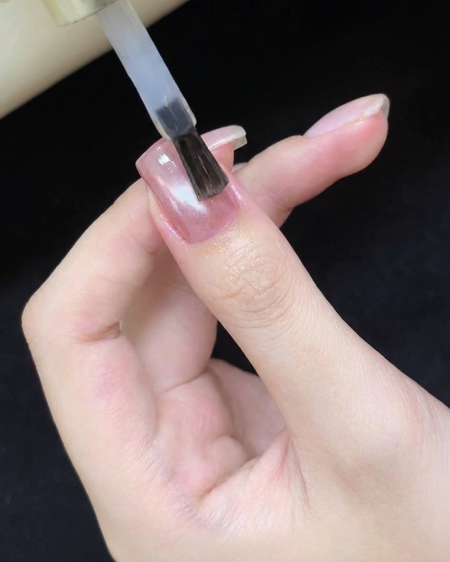 큐어링된 캣츠아이 네일 디자인 위에 투명하고 광택 있는 탑코트를 바르는 브러시.