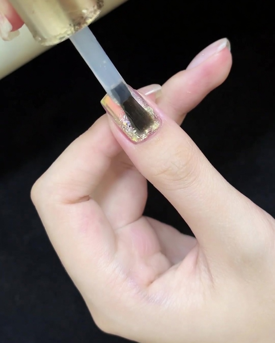 완성된 글리터 및 캣츠아이 네일 디자인 위에 투명하고 광택 있는 탑코트를 바르는 브러시.