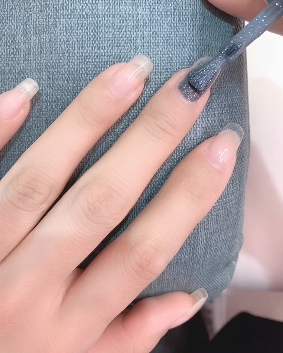 깔끔하게 정리된 손톱 위에 연한 그레이 컬러의 젤 폴리시를 브러시로 바르는 모습.