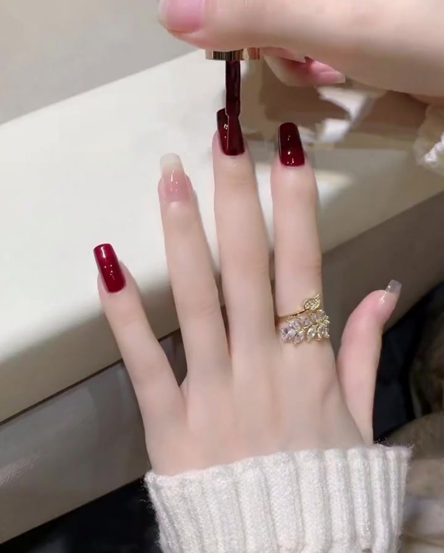 다크 와인 레드 젤 폴리시를 브러시로 엄지손톱에 얇게 바르는 모습.