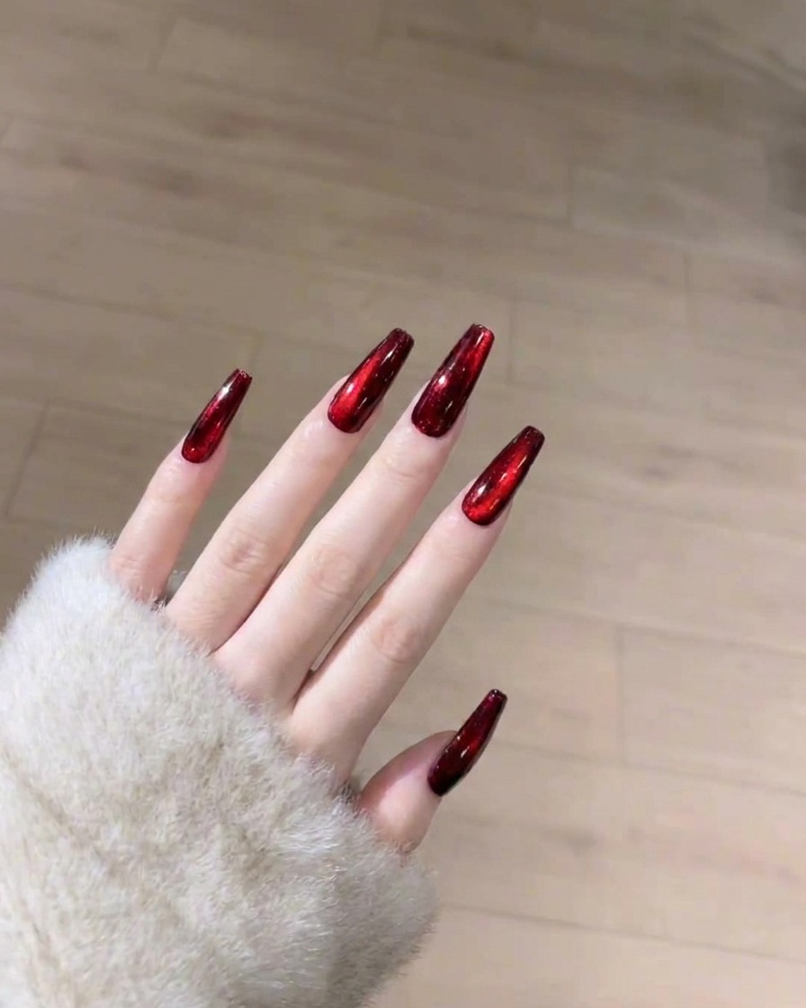 큐어링된 레드 캣아이 네일 위에 투명한 탑 코트를 바르는 모습.
