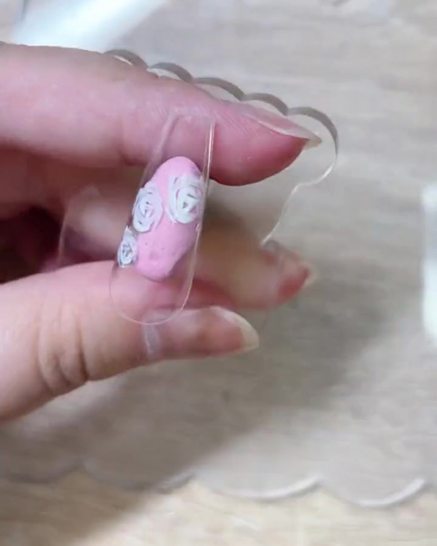 표면 전체에 펼쳐진 완성된 화이트 장미 꽃잎 아웃라인을 보여주는 네일 팁의 위에서 본 뷰.