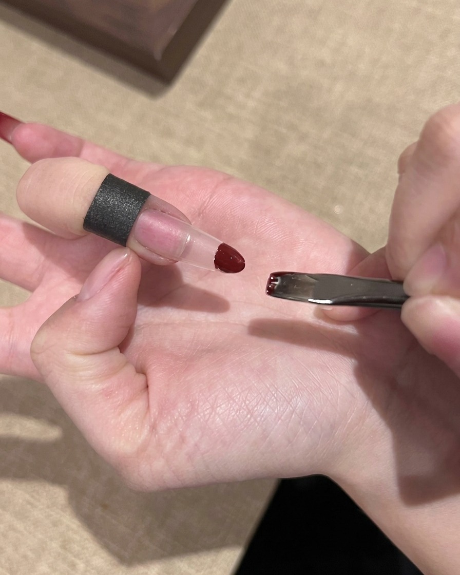 작은 스펀지를 사용하여 투명한 네일 연장 팁에 레드 젤 폴리시를 톡톡 두드려 바르는 손.