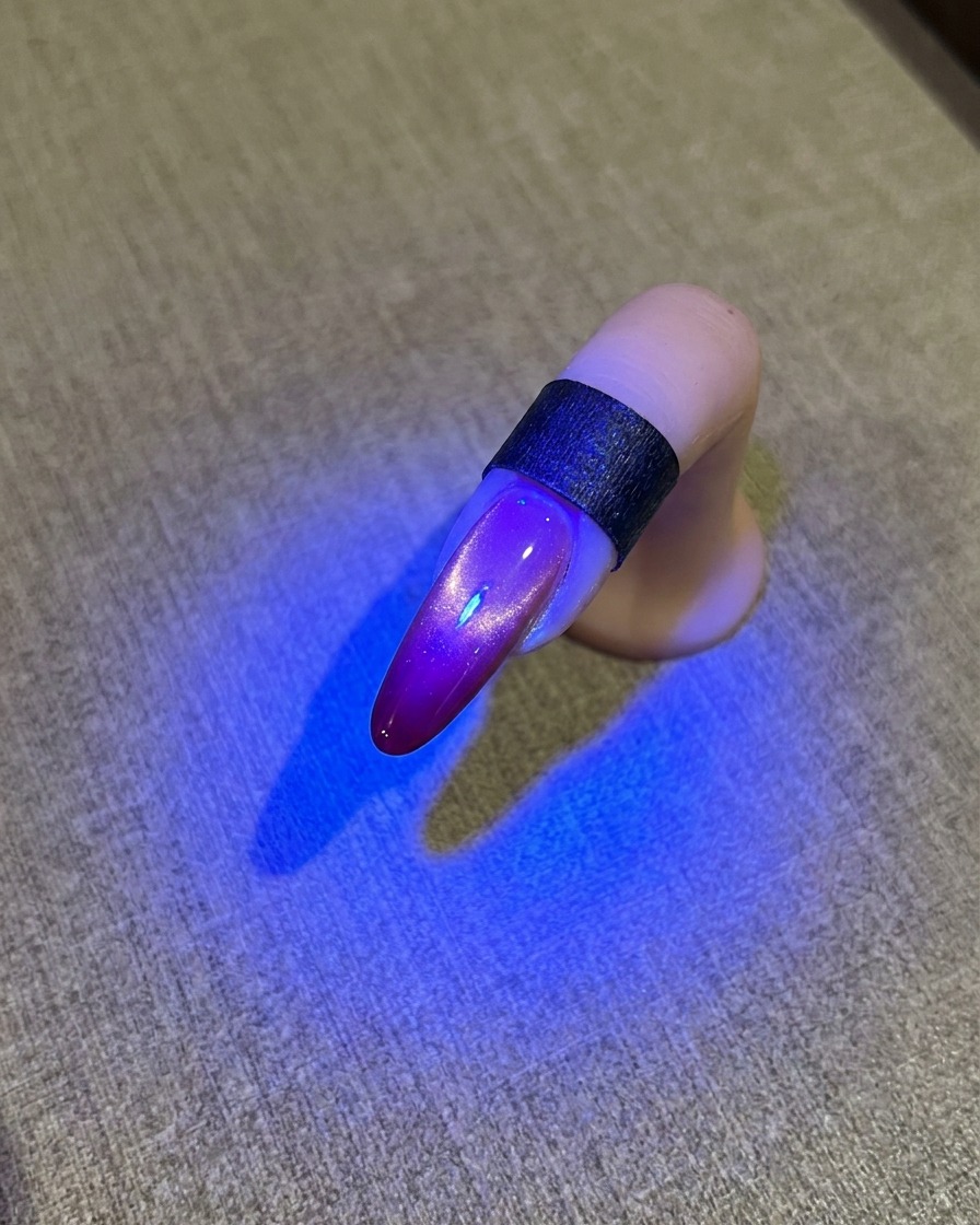 글로시한 자석젤 마무리가 보이는 블루 UV 램프 아래의 손톱.