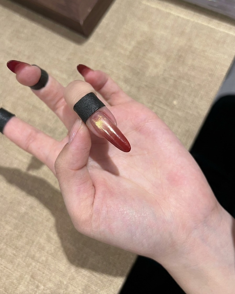 골드 포인트가 들어간 완성된 레드 그라데이션 자석젤 네일을 손에 얹어 보여주는 모습.