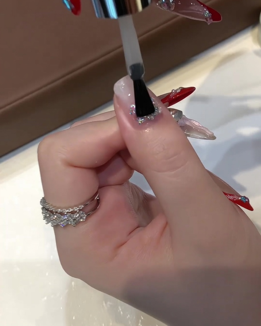 납작한 젤 브러시로 글리터가 올라간 손톱 위에 투명한 레벨링 빌더 젤을 두껍게 바르는 모습.