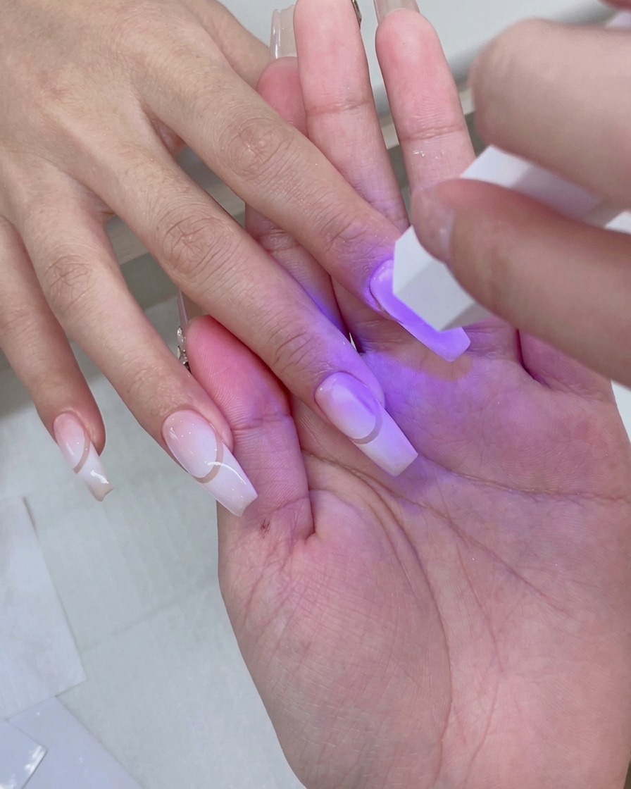 보라빛 불빛이 비치는 핑크빛 UV/LED 네일 램프 안에 프렙된 그라데이션 네일을 마친 손을 넣고 있는 모습.