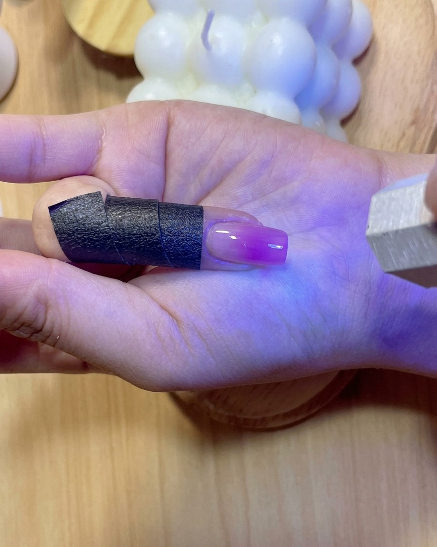 보라색 UV/LED 빛 아래에서 reinforcement 젤이 발린 손톱이 반짝이며 경화되는 모습.