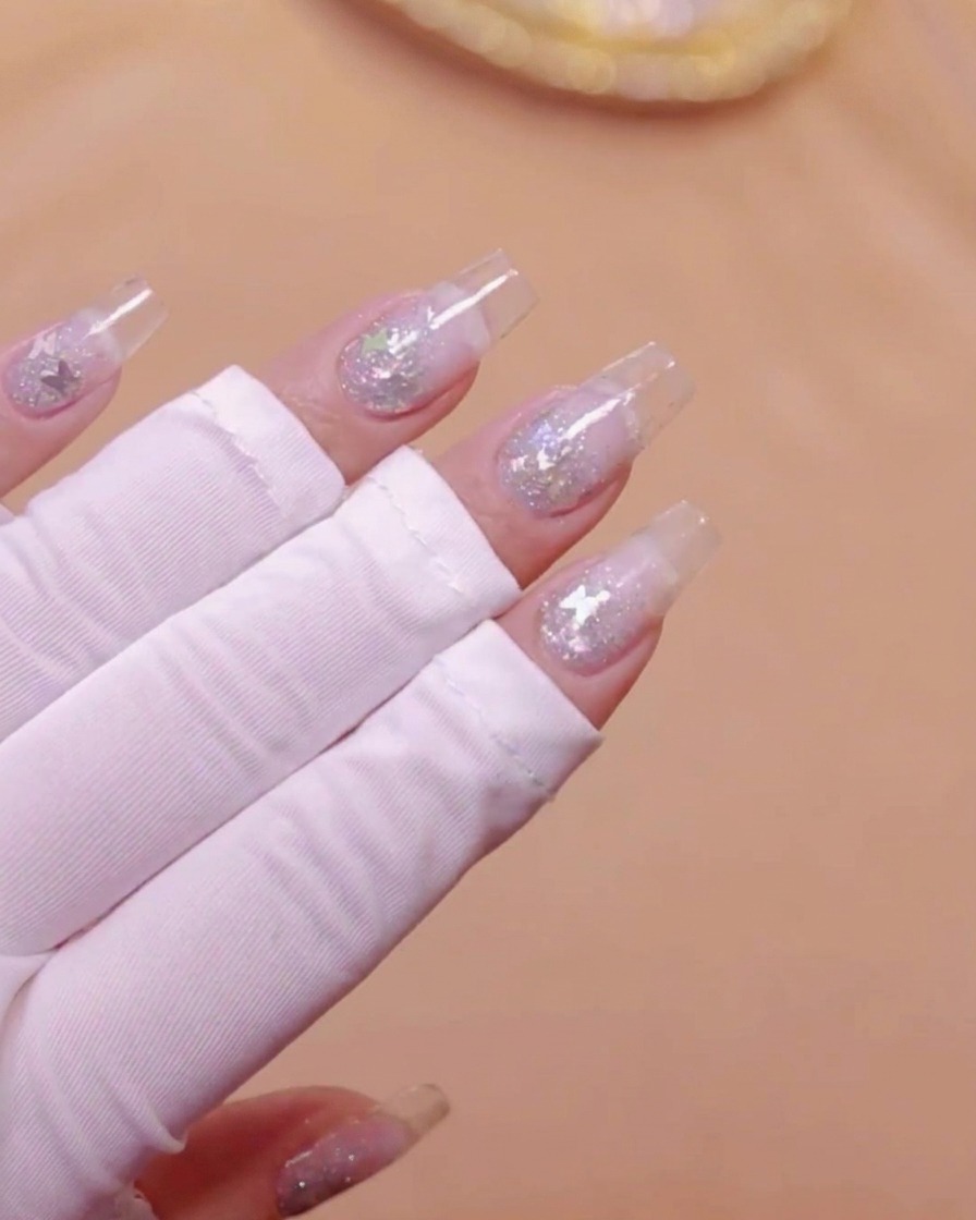 투명 연장 네일과 나비 글리터가 장식된 손을 UV 램프 아래에 둔 모습.