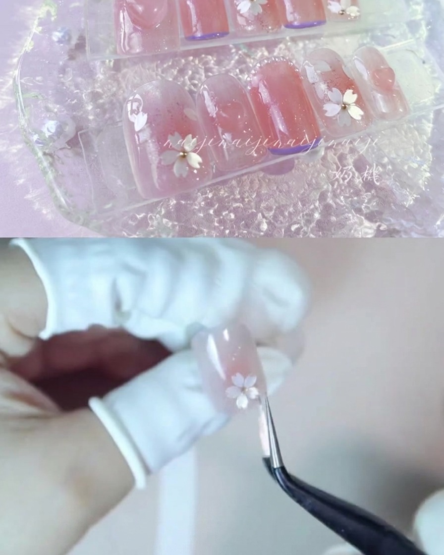 정밀 핀셋으로 화이트 벚꽃 잎 조각을 광택 나는 손톱 위에 조심스럽게 올리는 모습.