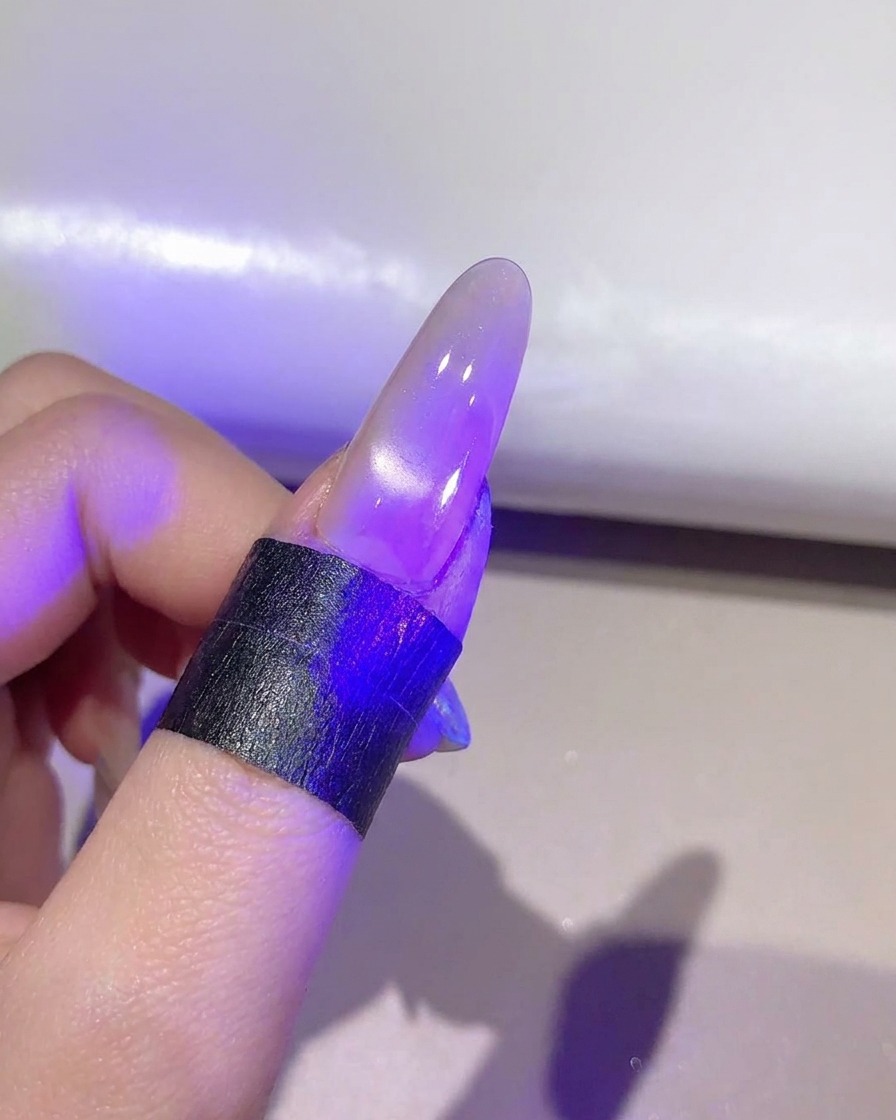 완성된 캣아이 젤 레이어를 보라색 UV/LED 램프 아래에서 경화하는 네일.