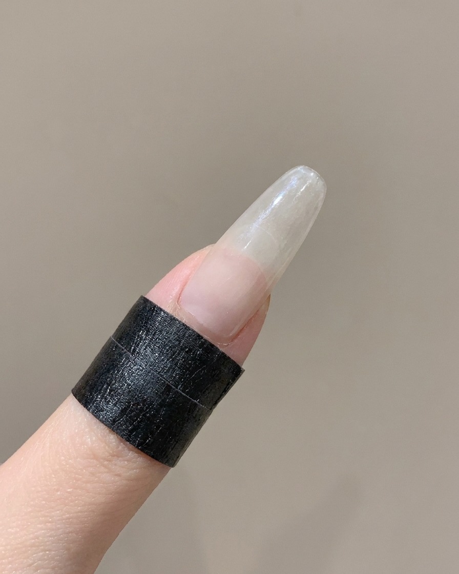 흰색 앵글 실리콘 툴로 손가락의 곡선형 프렌치 네일 스티커 가장자리를 누르는 모습.