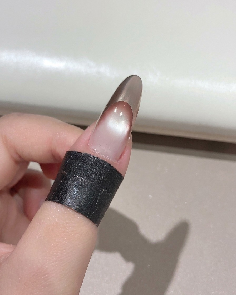 완성된 골드 로즈 프렌치 매니큐어 위에 네일 브러시로 클리어 글로시 탑 코트를 바르는 모습.