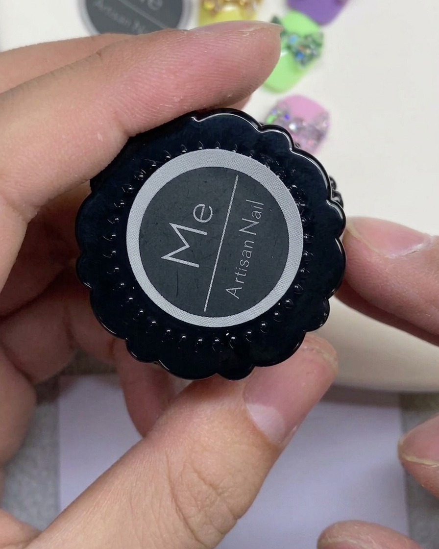흰색 원형 로고가 있는 Artisan Nail이라는 검은색 용기를 들고 있는 손.