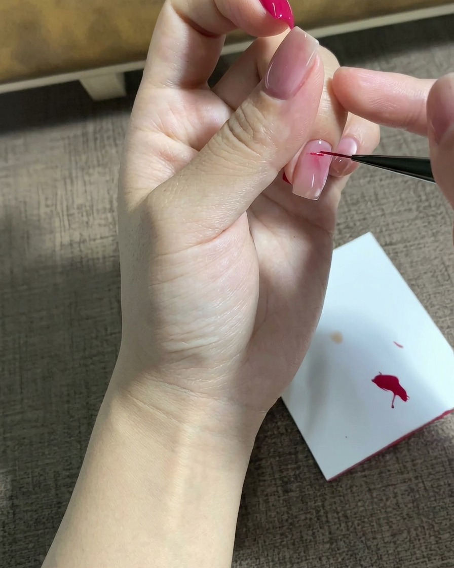 파인 라이너 브러시로 사전 작업된 네일 표면 위에 디테일한 마젠타 색상의 별 모티브를 그리는 모습.