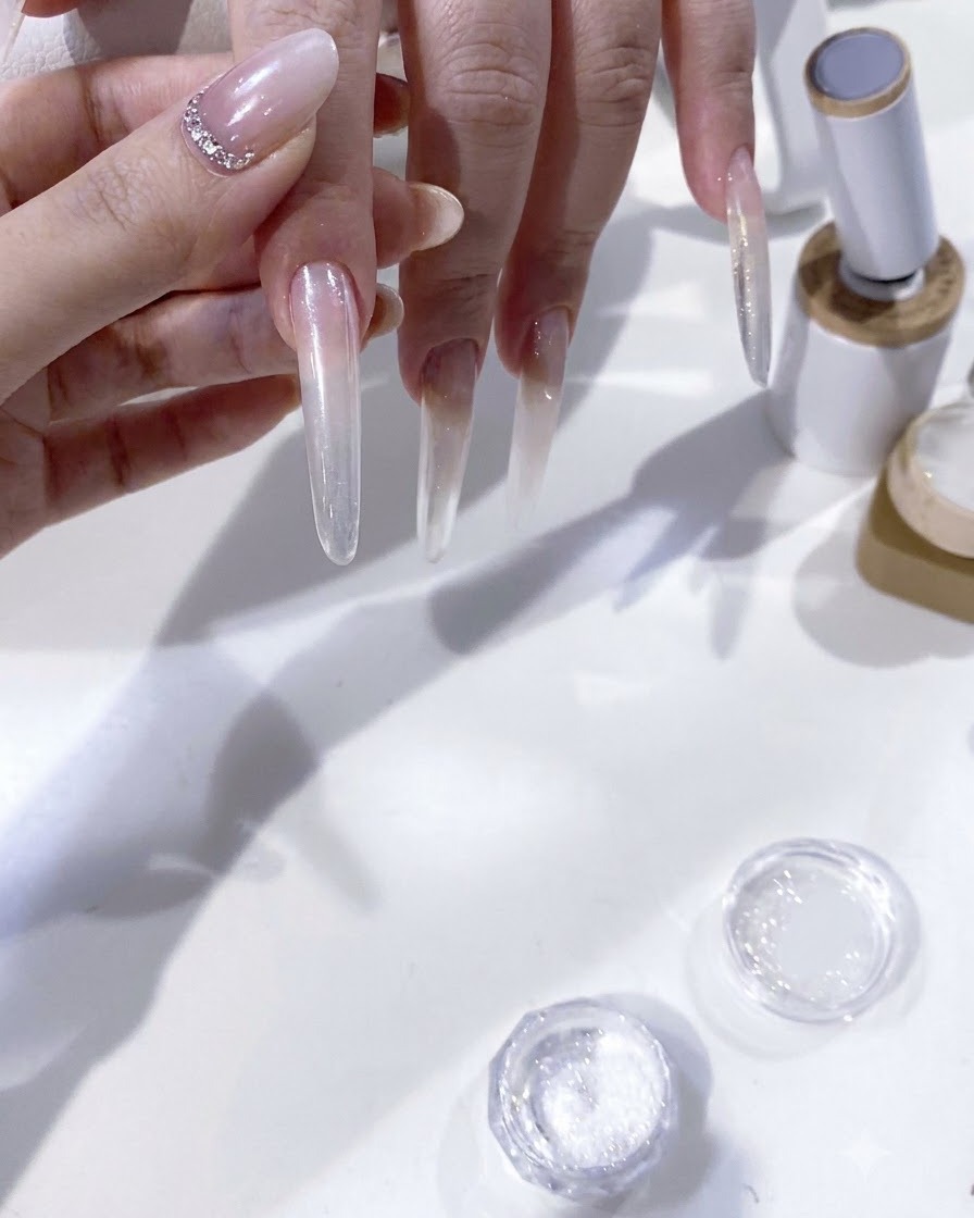 연장된 네일에 프렌치 팁을 만들기 위해 브러시로 화이트 젤 피그먼트를 신중하게 바르는 클로즈업 뷰.