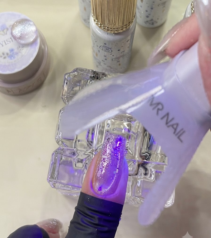 보라색 빛 아래에서 장식된 네일을 큐어링하는 미니 UV 램프.