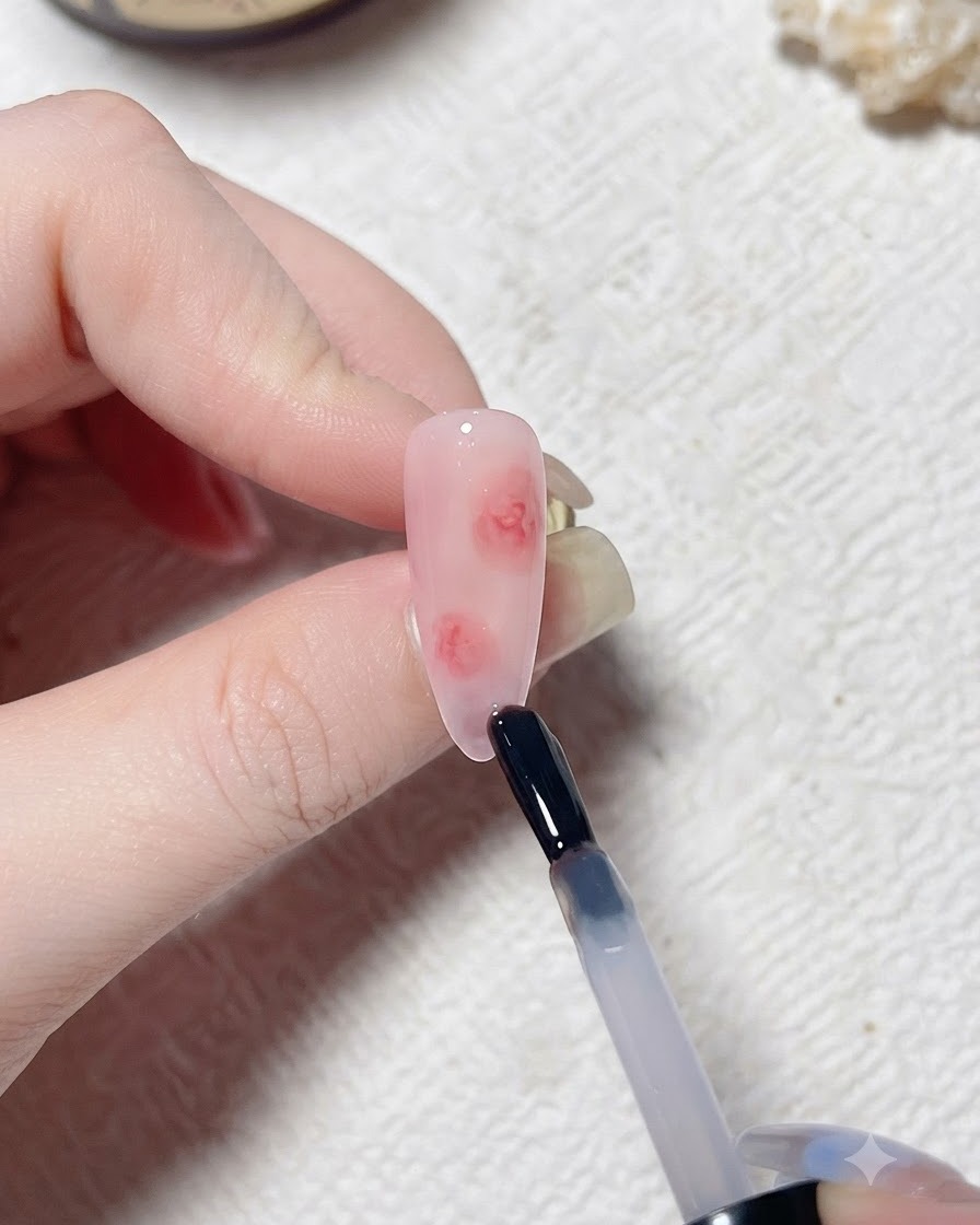 핑크 톤의 인조 손톱 위에 브러시가 투명한 블루밍젤 층을 바르고 있는 모습.