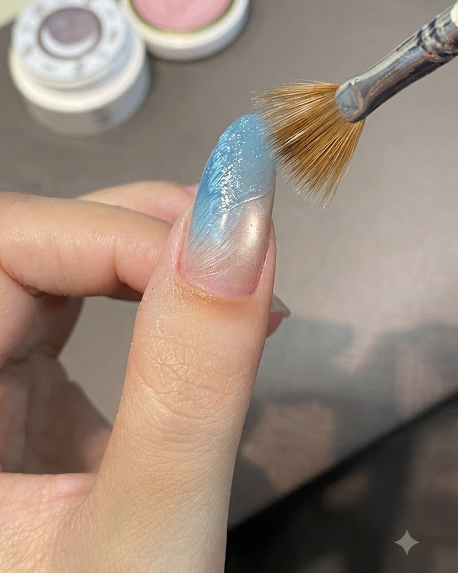 블루 그라데이션 손톱 위의 젖은 스컬프팅 젤을 대각선 방향으로 쓸어 넘겨 솟아오른 릿지를 만드는 스트라이핑 브러시의 모습.