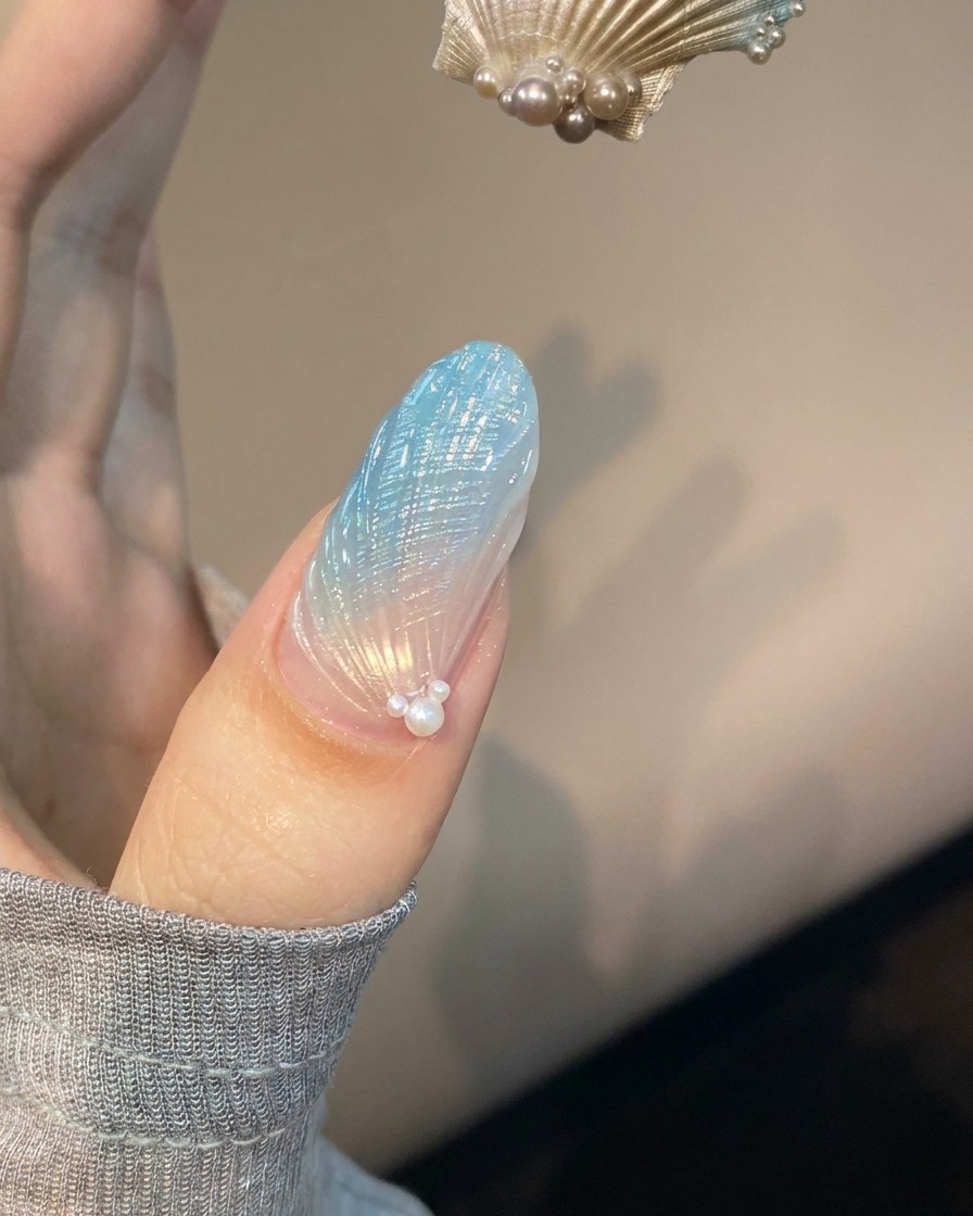 블루 및 투명 쉘 네일아트가 적용된 손톱이 보라색 UV 램프 아래에서 경화되는 모습.