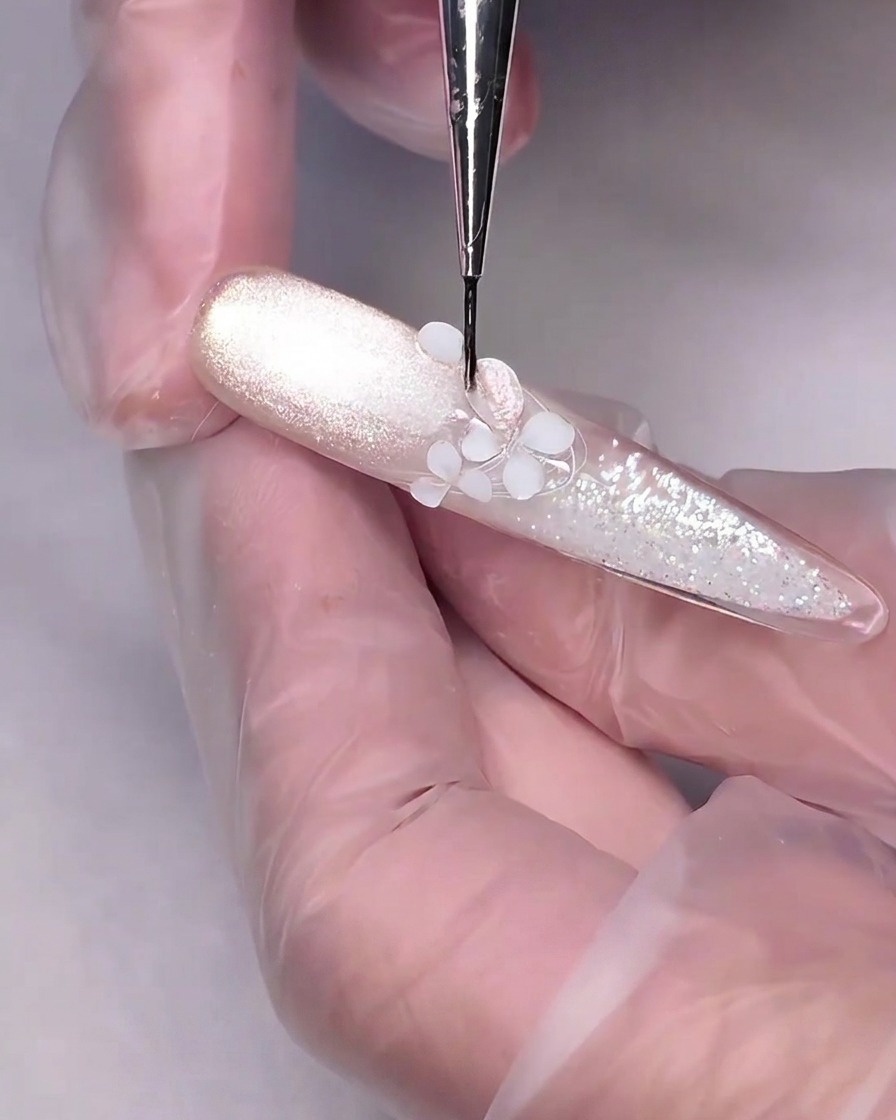 파인 디테일링 브러시가 네일의 흰색 3D 조각 꽃 위에 누드 핑크 자석 젤을 바르고 있는 모습.