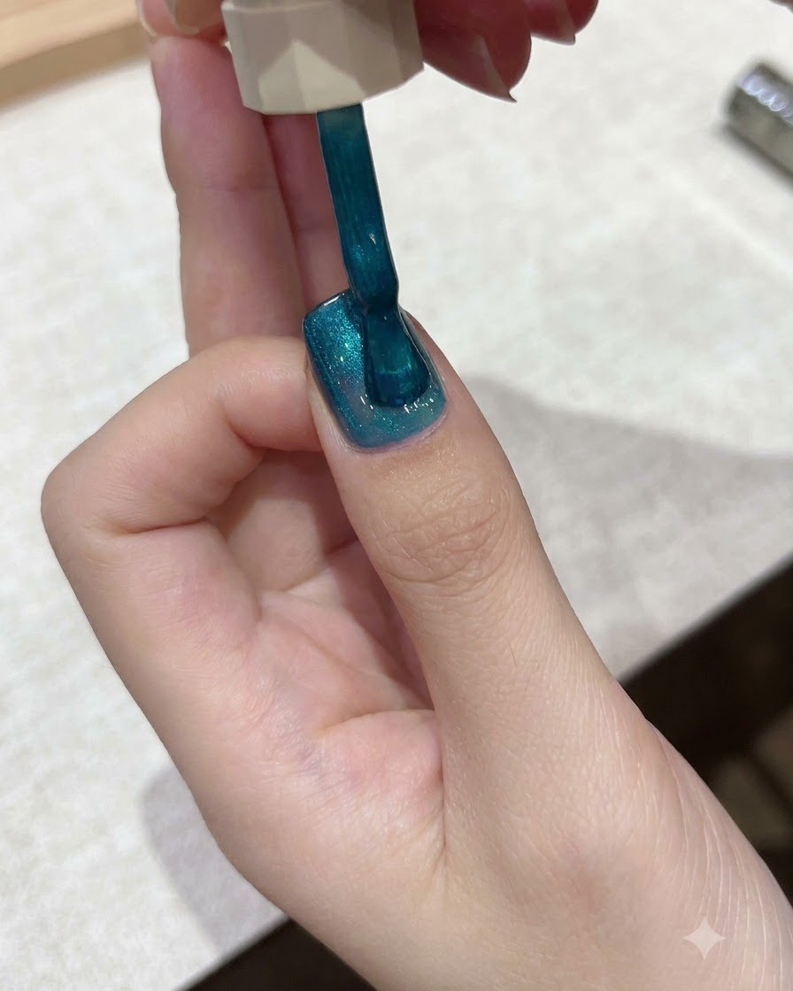 브러시가 손톱 표면 전체에 생동감 있는 틸 블루 자석 젤 폴리시를 펴 바르는 모습.