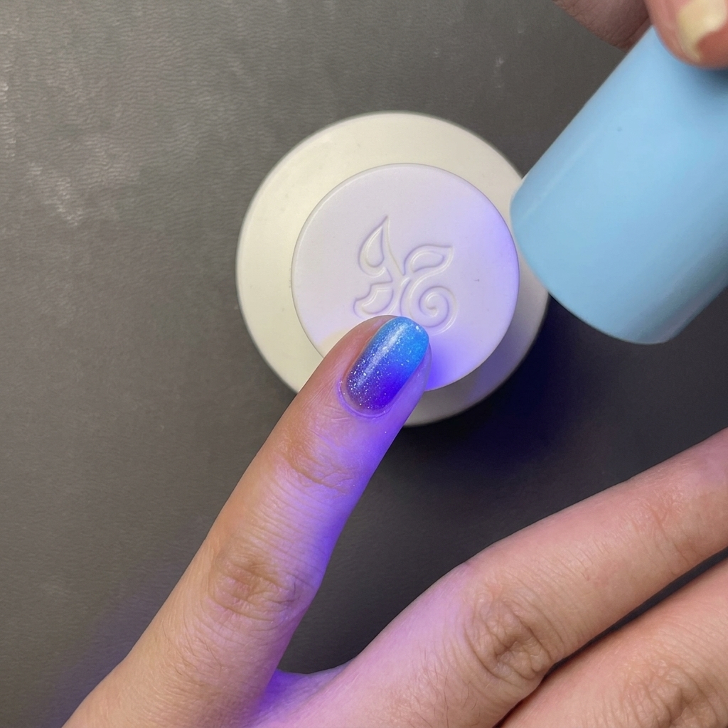 작고 휴대 가능한 하늘색 UV/LED 램프 아래에서 밝은 파란색 젤 폴리시가 칠해진 손가락이 경화되는 모습.