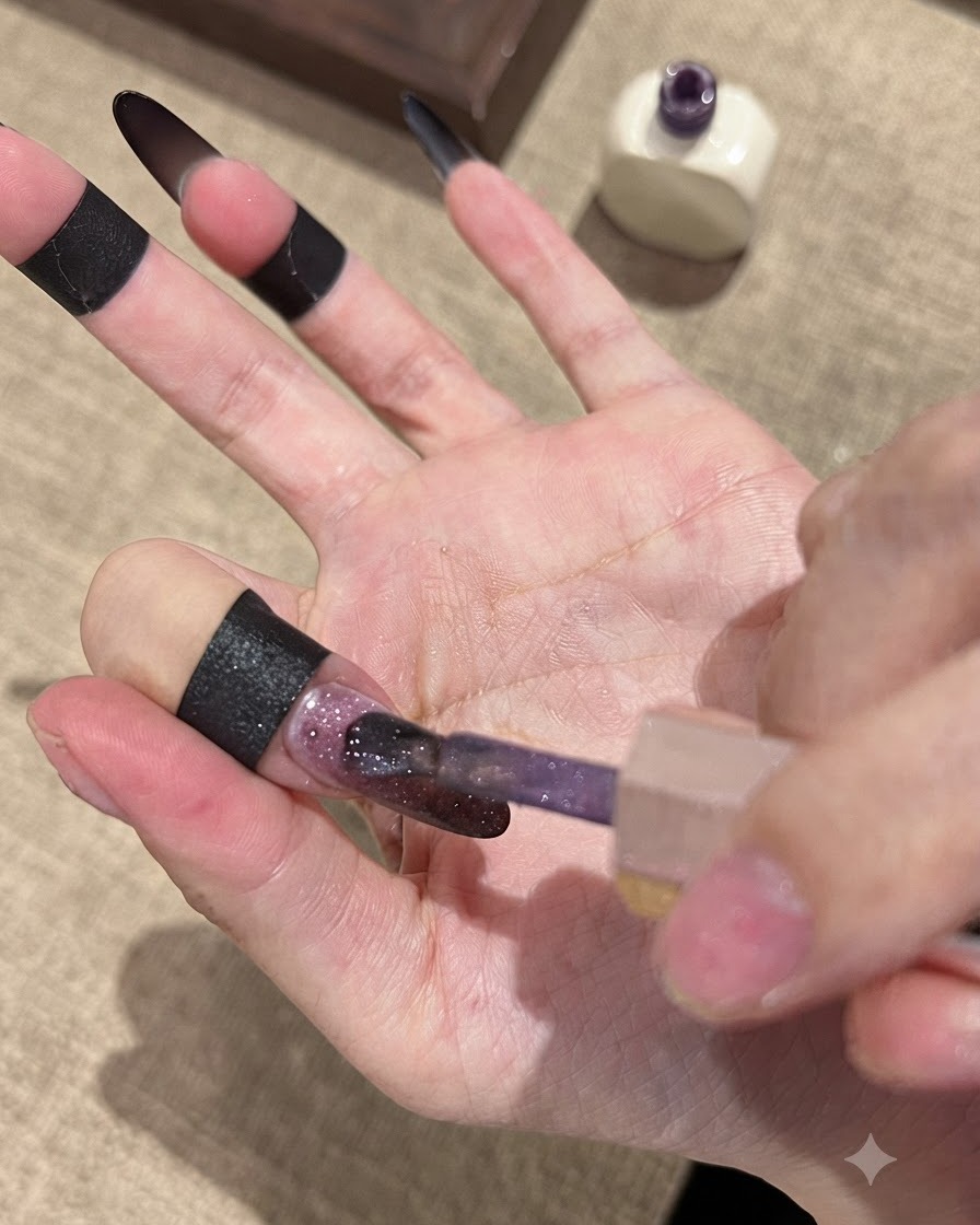 브러시가 다크 그라데이션 네일 베이스 위에 폴른 골드 캣아이 젤 폴리시를 바르고 있는 모습.