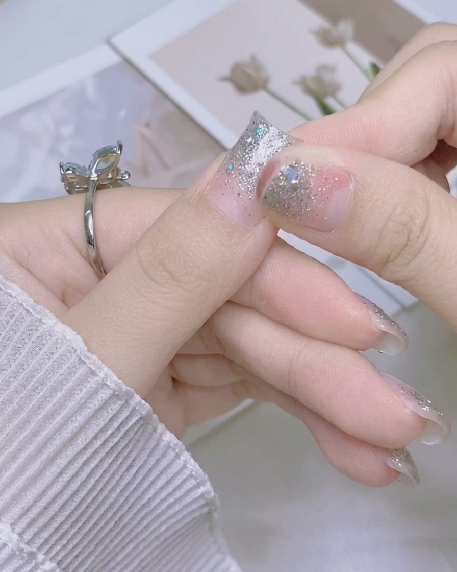 반짝이는 실버 네일 스티커의 남은 길이를 엄지손톱 가장자리 아래쪽으로 단단히 접어 내리는 손.