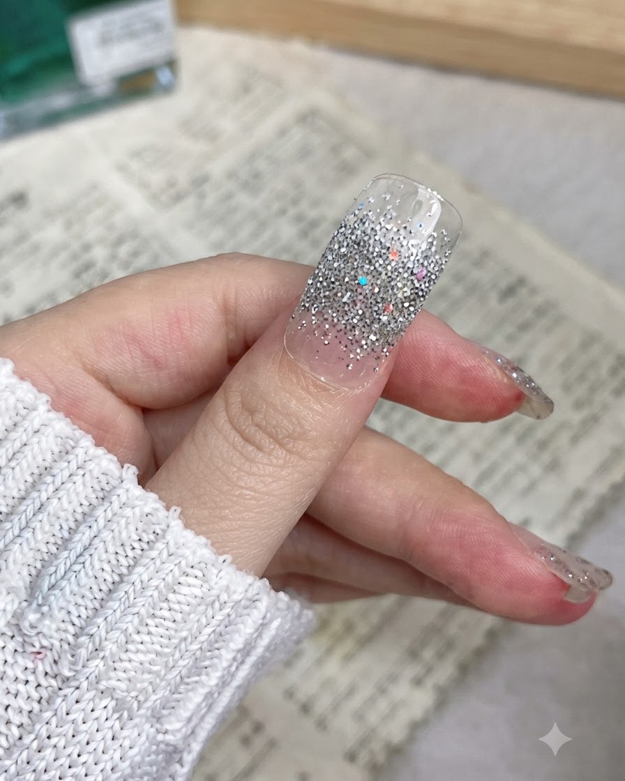 큐티클부터 엣지까지 매끄럽게 부착된 실버 글리터 네일랩 엄지손가락 클로즈업.