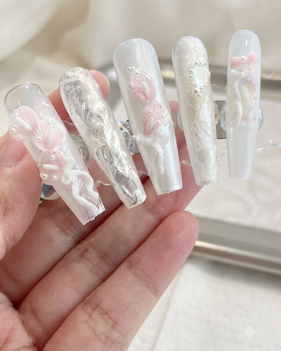 중립적인 배경 속에서 3D 칼라릴리, 리본, 진주 장식이 돋보이는 완성된 프레스온 네일 디스플레이.