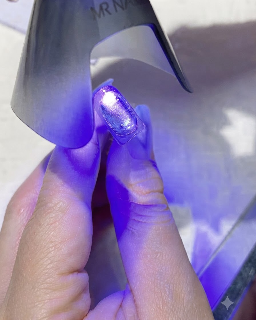 미니 보라색 핸드헬드 UV/LED 네일 램프가 코팅된 네일 바로 위에서 보라색 빛을 발산하는 모습.