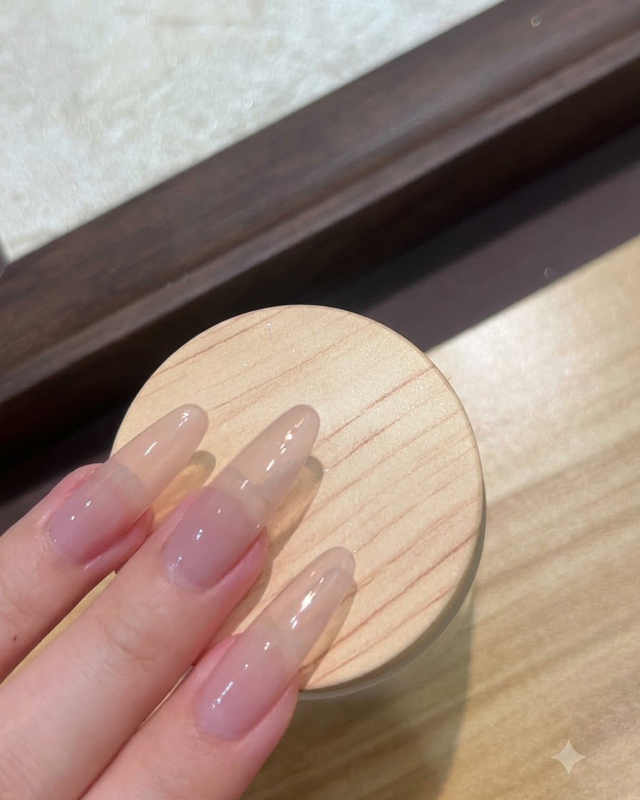 클리어 베이스 젤 레이어로 프렙 중인 롱 누드 연장 네일의 클로즈업 뷰.