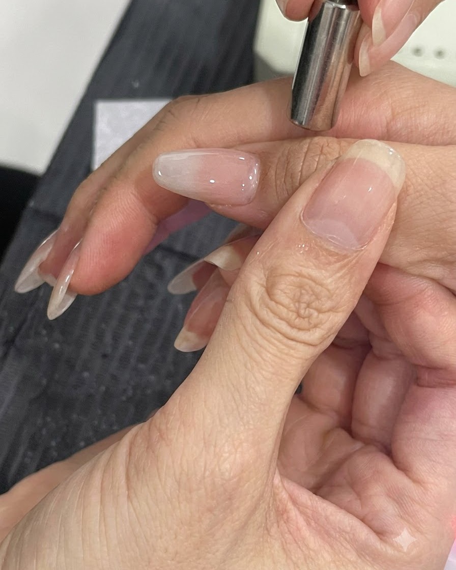 작은 자석 도구가 매니큐어 처리된 네일 측면에 가까이 대어져 자석 펄 입자를 이동시키는 모습.