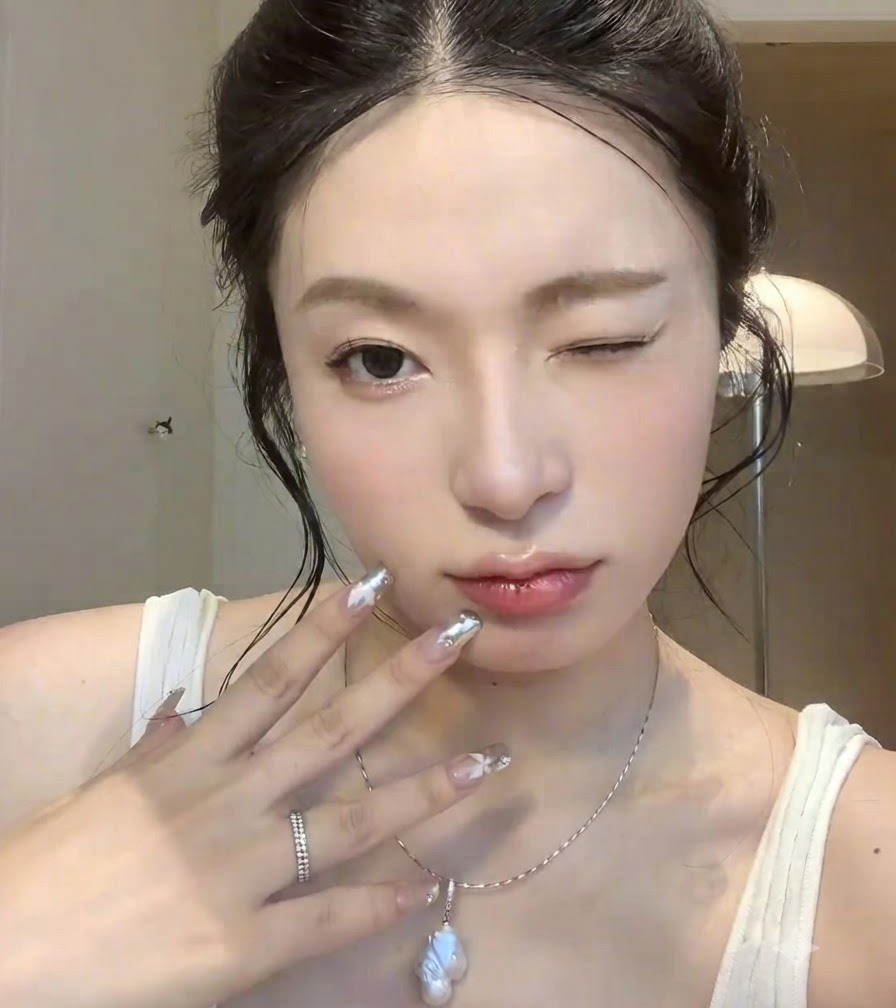 윙크하는 표정과 함께 얼굴 가까이에 실버 크롬 네일 아트를 든 손의 클로즈업.