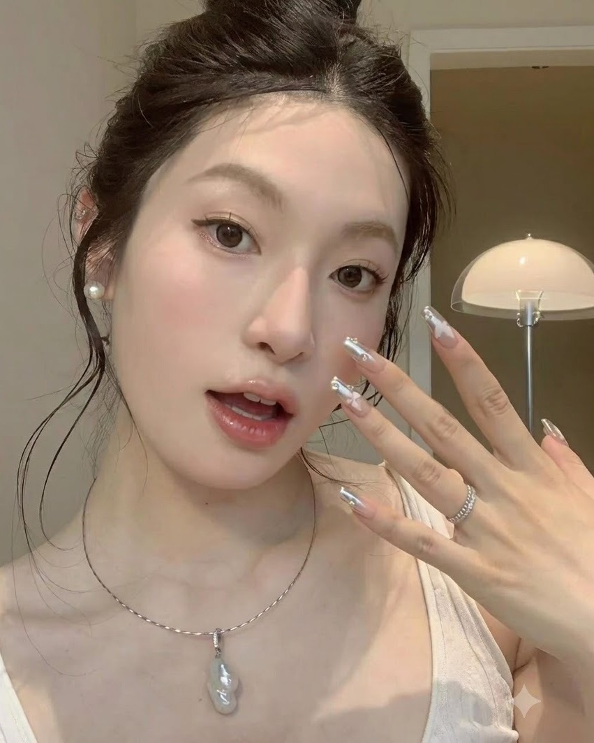 나비 장식이 있는 실버 크롬 네일을 강조하며 뺨에 가볍게 갖다 댄 손의 안정적인 클로즈업 샷.