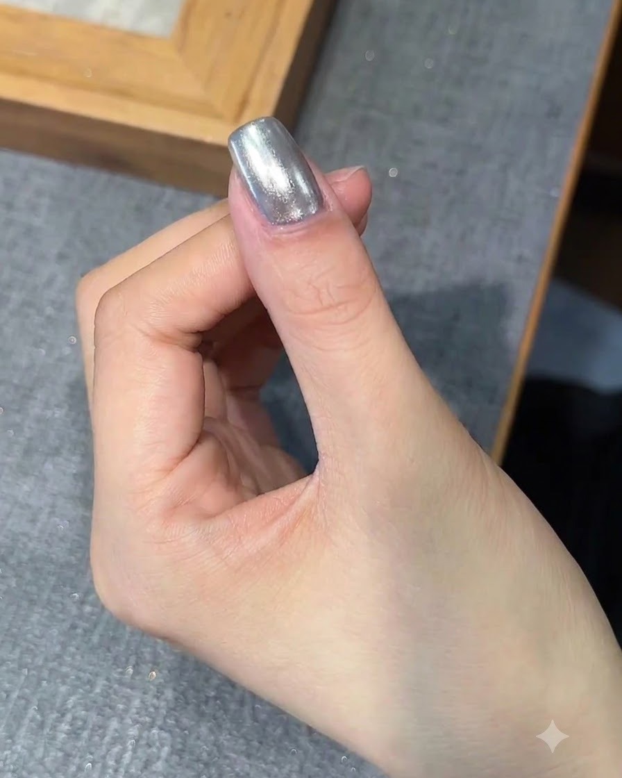 브러시가 크롬 피니시가 완료된 손톱 위에 베이스 젤 한 콧을 바르고 있는 모습.
