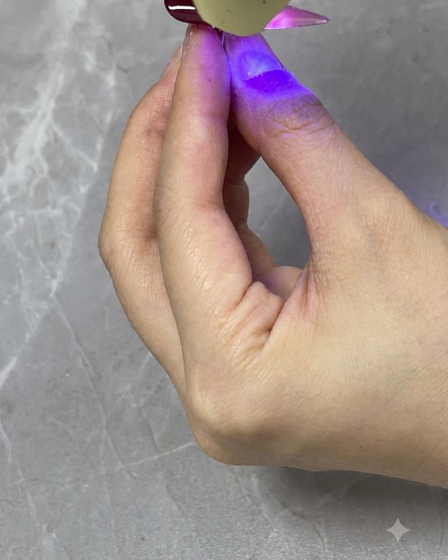 완성된 네일의 반투명 레드 그라데이션 레이어를 큐어링하는 휴대용 UV/LED 램프.