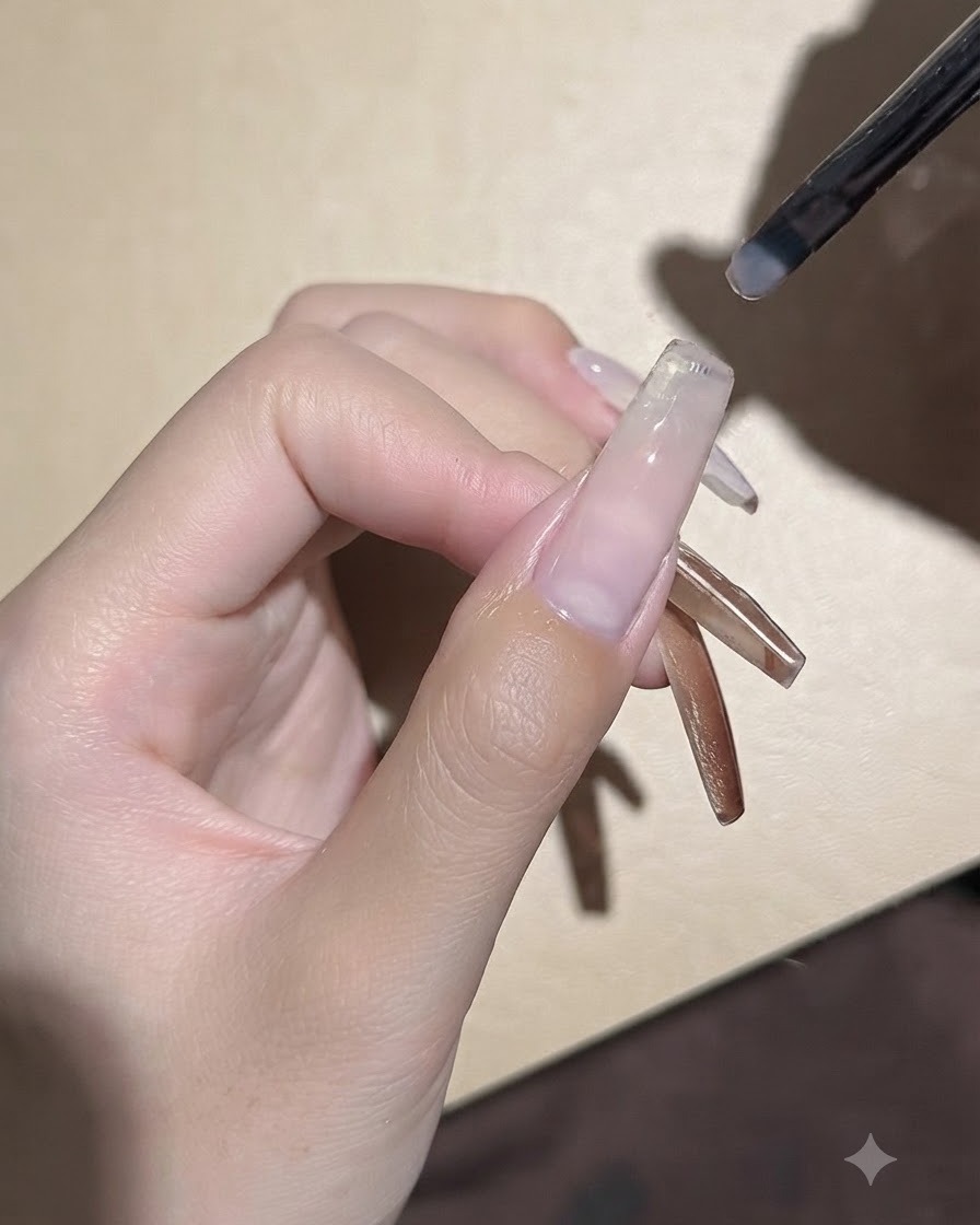 작은 젤 브러시가 전처리된 네일 바디 위에 매끄럽게 클리어 베이스 젤을 펴 바르는 모습.