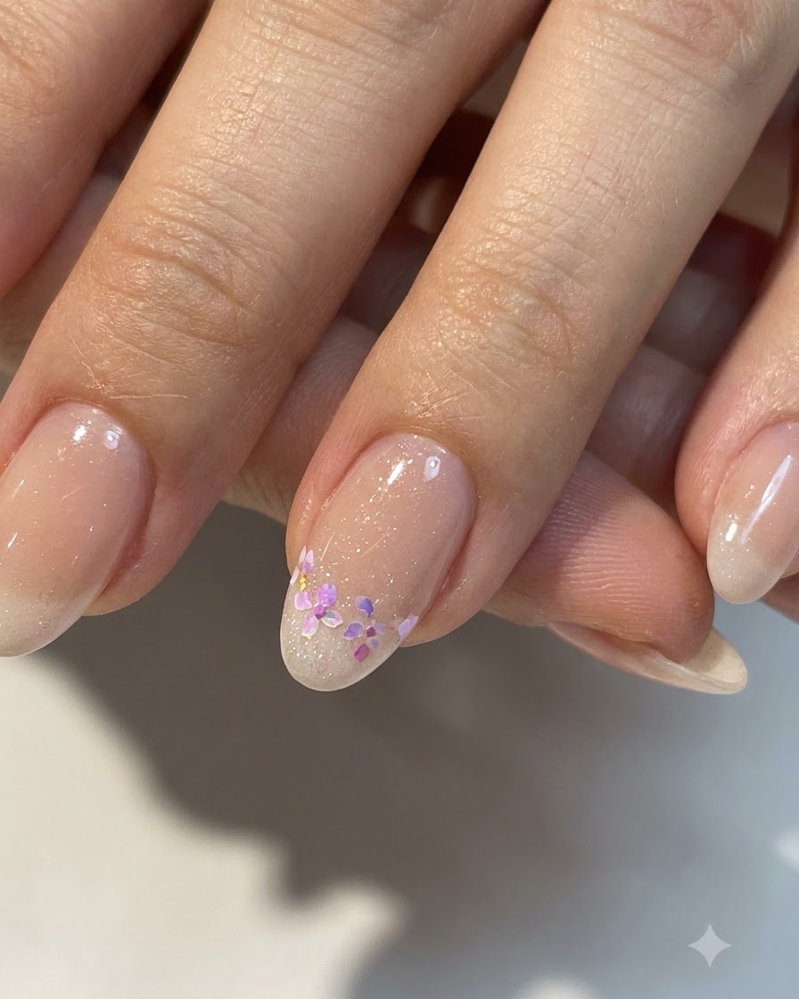 Eine Nahaufnahme von vollendeter kleiner Blumen-Nagelkunst auf einer glänzenden Nude-Basis mit verfeinerten Details.