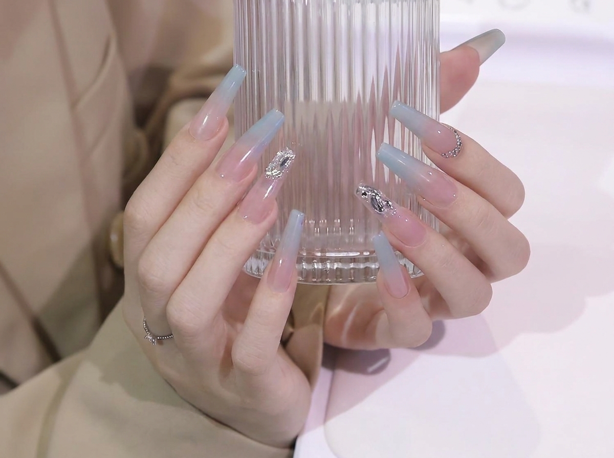 유리 컵을 잡는 그립을 살짝 조절하여 긴 코핀 네일의 부드러운 블루 투 누드 그라데이션 변화를 보여주는 모습.