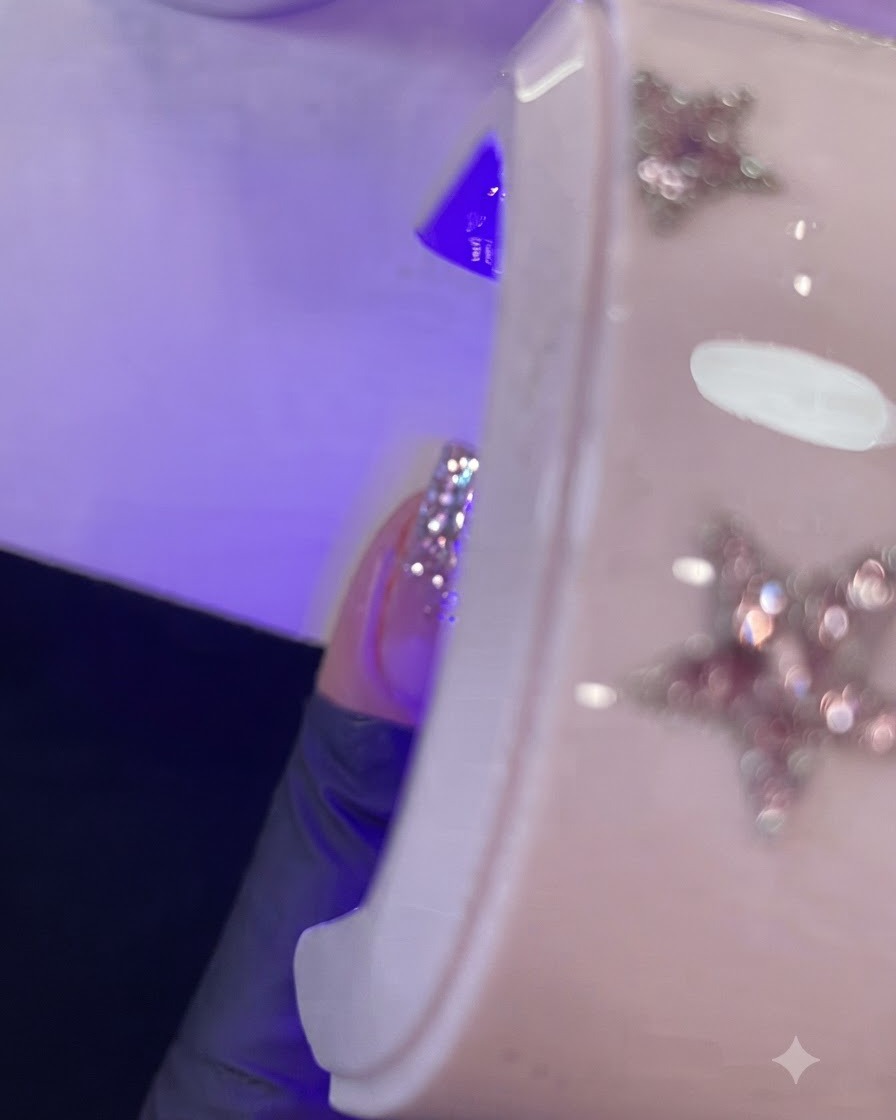 젖은 젤이 칠해진 손가락이 보라색 미니 UV/LED 램프 아래에서 큐어링되는 클로즈업.