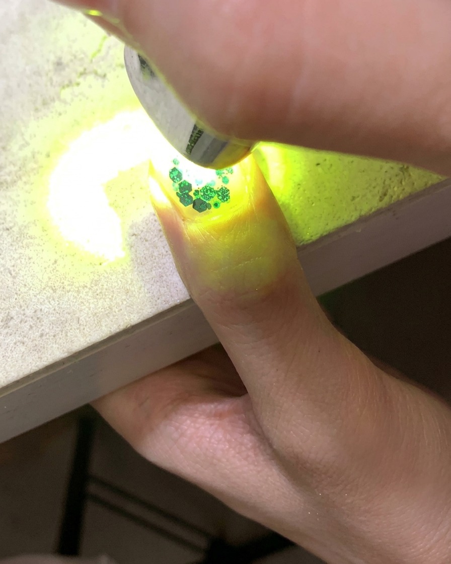 글리터와 속이 빈 별 모양 스팽글로 장식된 손톱을 큐어링하는 미니 UV 램프.