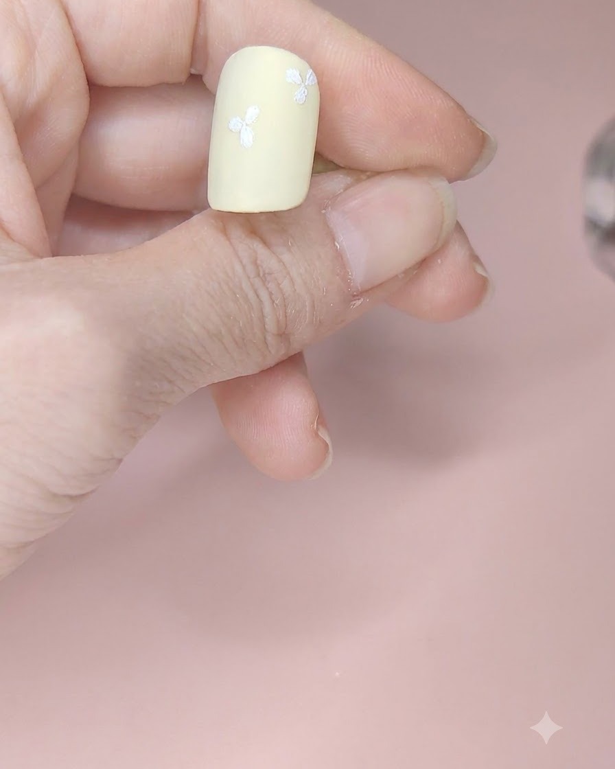 네일 표면 곳곳에 네 개의 흰색 세 잎 꽃이 배치된 페일 옐로우 네일.