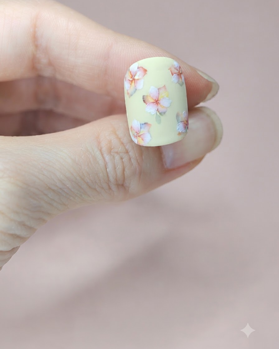 중앙 꽃 무리 옆에 작은 초록색 수채화 잎이 그려진 페일 옐로우 네일 클로즈업.