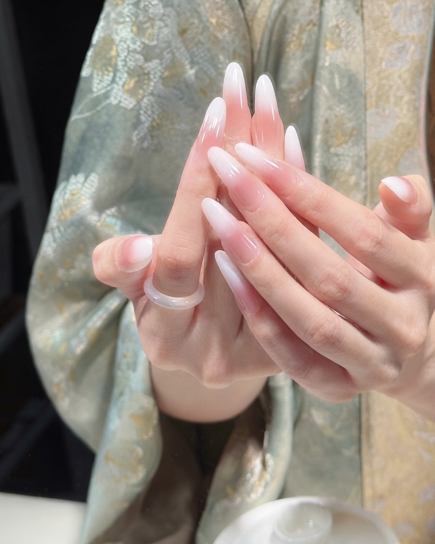 완성된 핑크 앤 화이트 그라데이션 네일 위에 투명하고 광택 있는 탑코트를 바르는 네일 브러시.