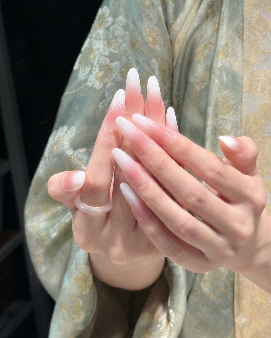 스튜디오 조명 아래에서 고광택 마무리를 뽐내는 완성된 긴 아몬드 쉐입의 핑크 앤 화이트 그라데이션 네일.