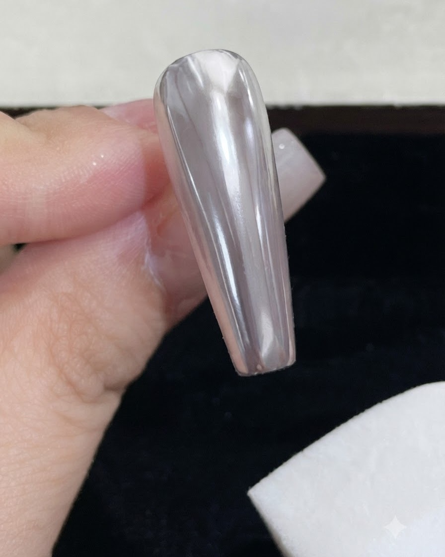 하얀색 폼 스펀지 블록으로 광택이 나는 크롬 네일의 잔여 미러 파우더를 닦아내는 모습.