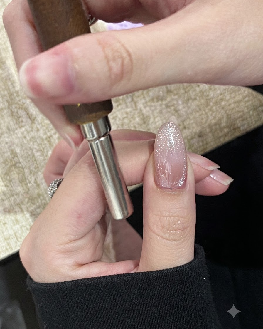 아직 경화되지 않은 반짝이는 자석 네일의 프리엣지 부분에 원통형 자석을 가로로 가까이 대는 모습.