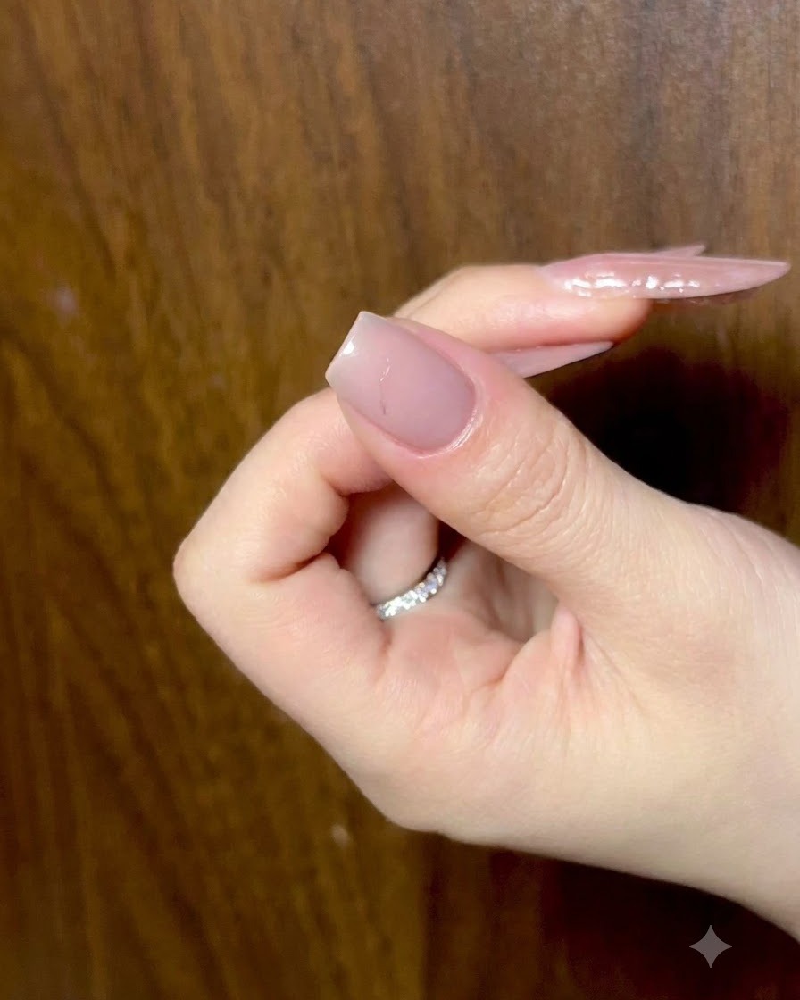 은은한 조명 아래 준비된 누드 네일을 보여주며 손가락을 살짝 구부린 채 쉬고 있는 손.